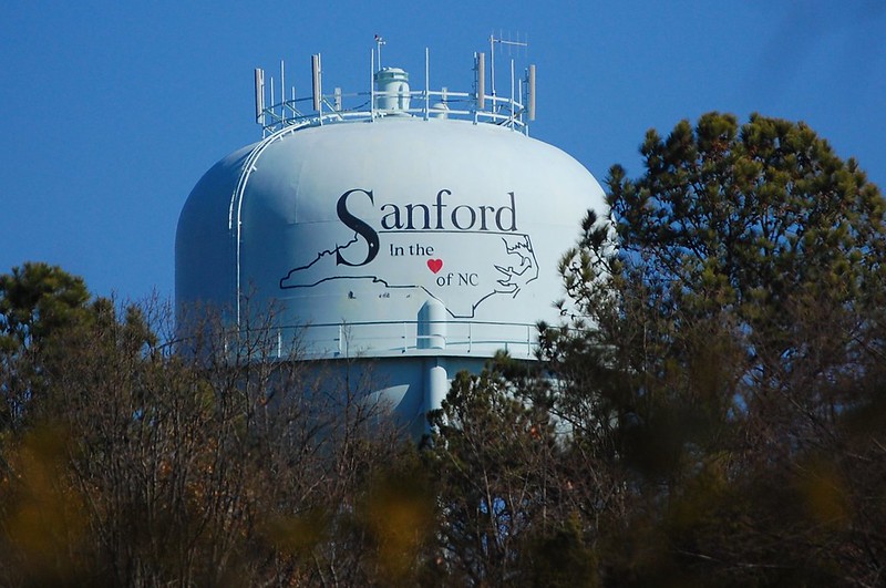 Sanford, NC, water tower with trees in foreground and blue sky in background.