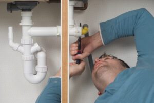 Plumber repairing a leak under a sink in an apartment.